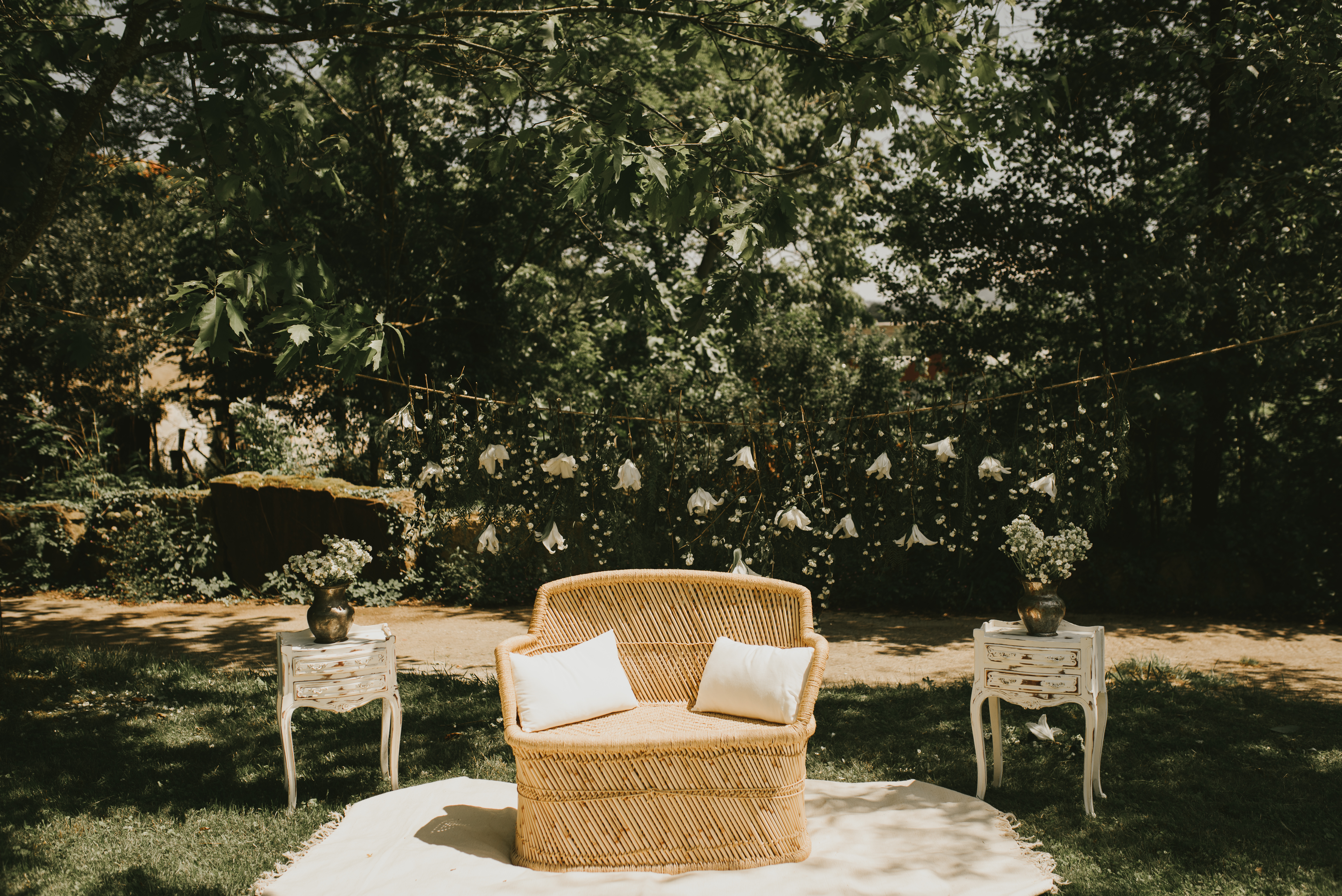 Altar nupcial con sillón doble de ratán, mesas auxiliares y alfombras en un entorno natural