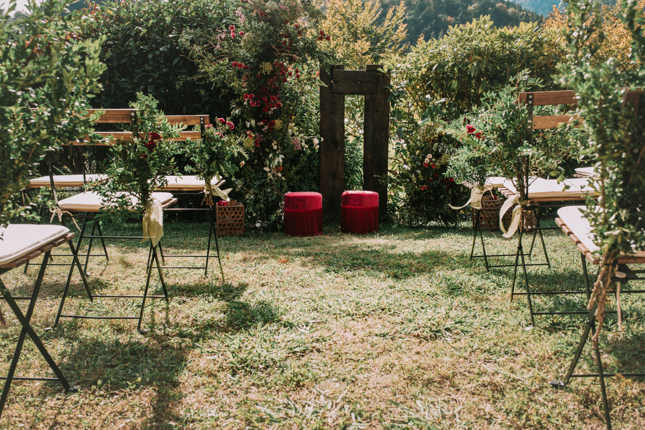 Ceremonia natural con puffs rojos, arco natural y sillas de forja y madera