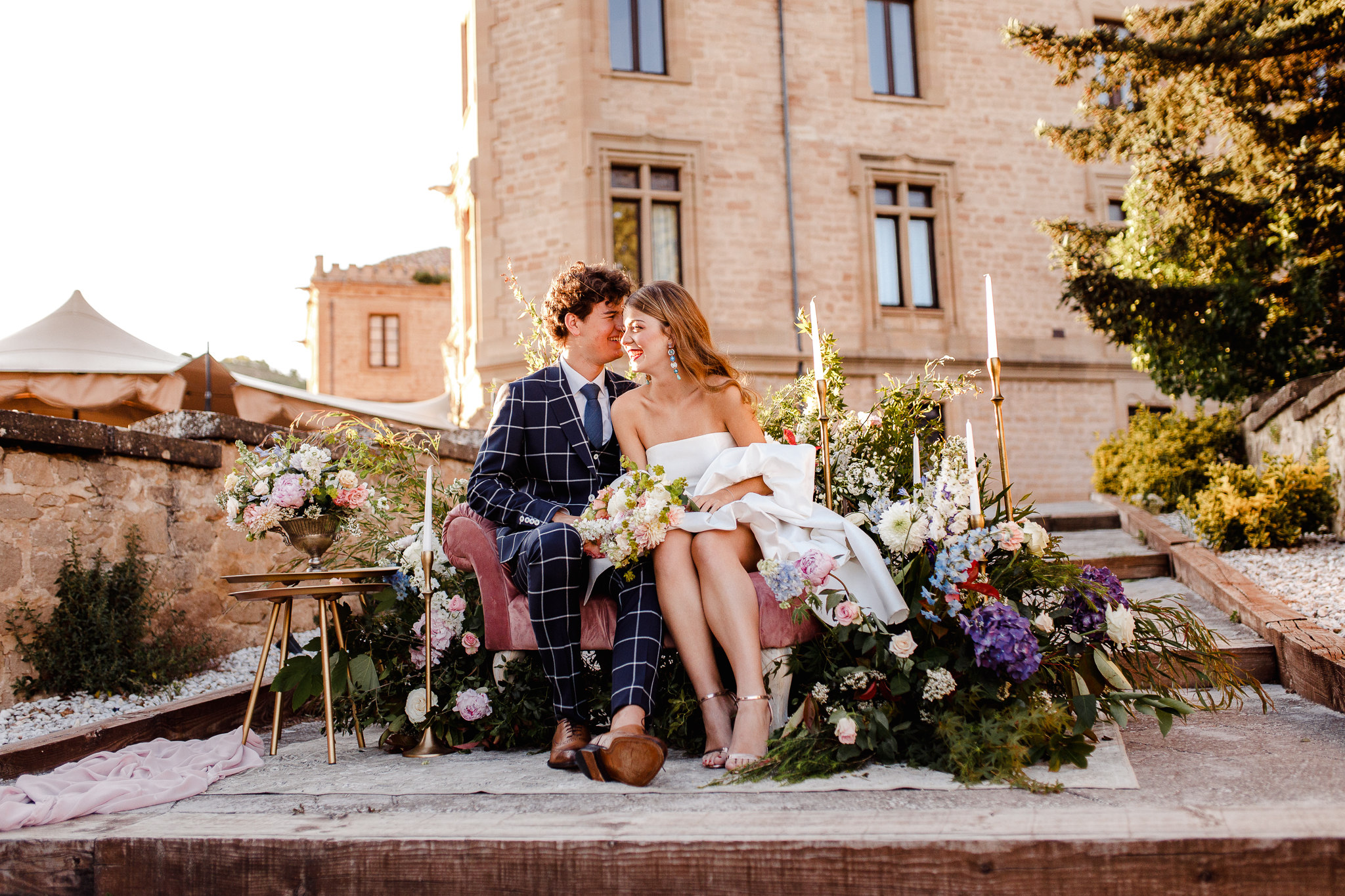 Novios sentados en sillón de terciopelo rosa, rodeado de decoración floral