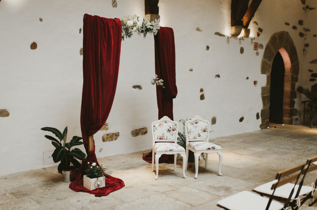 Arco con tela roja y sillas con estampado floral para la decoración de una ceremonia