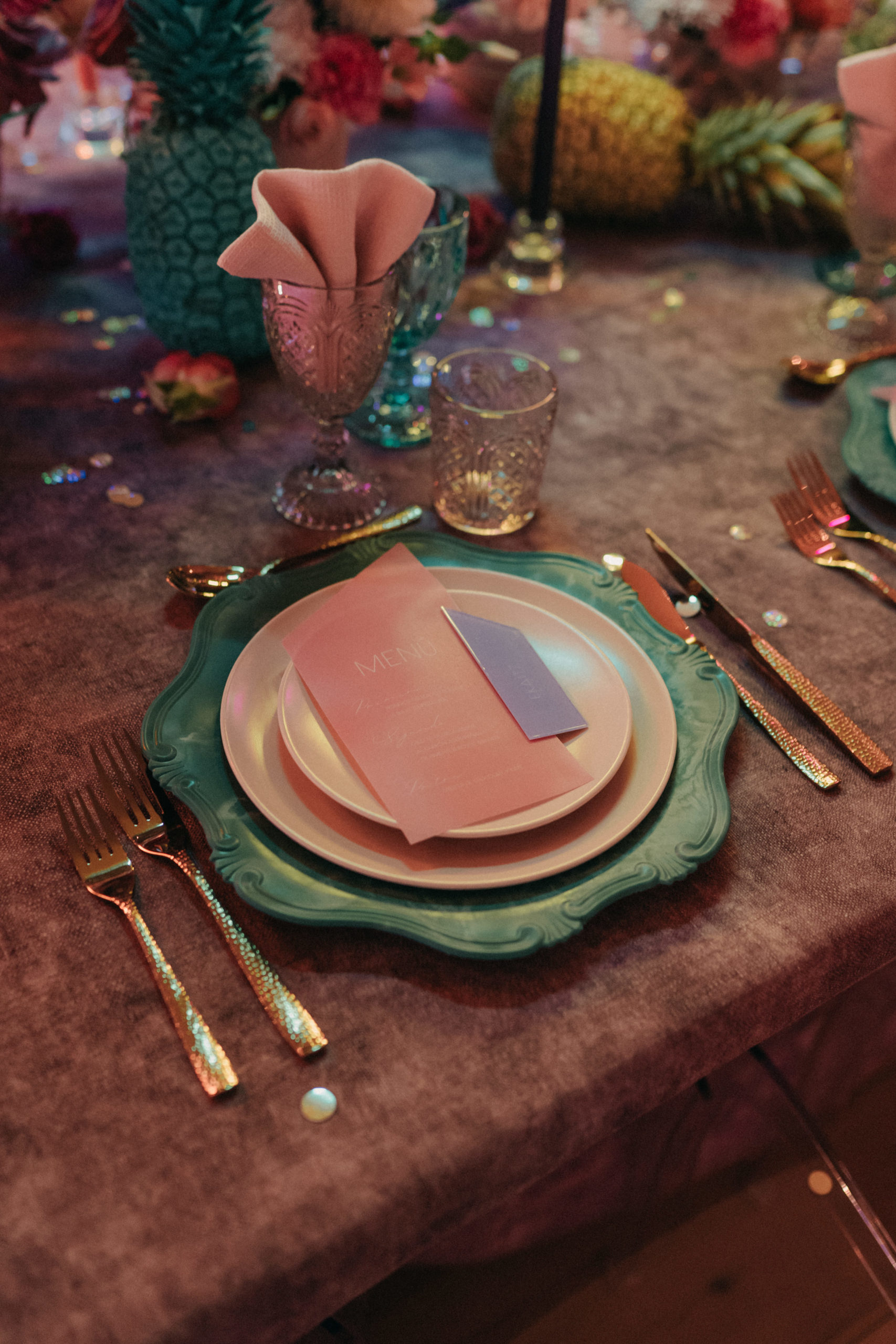 Bajoplato azul, cubertería dorada y copas azul turquesa y rosas en una mesa de banquete