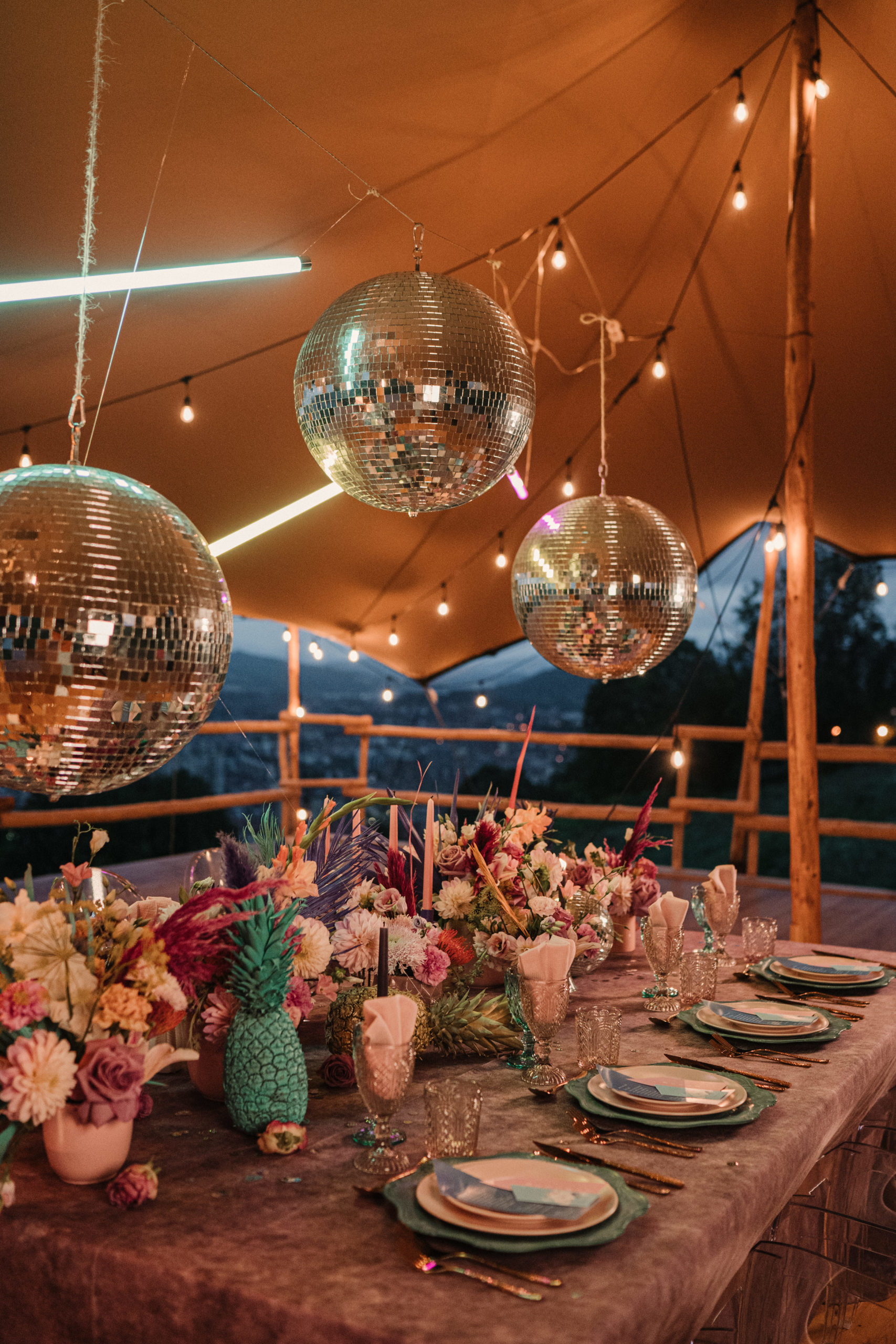 Bolas de discoteca sobre mesa nupcial llena de menaje y decoración colorida