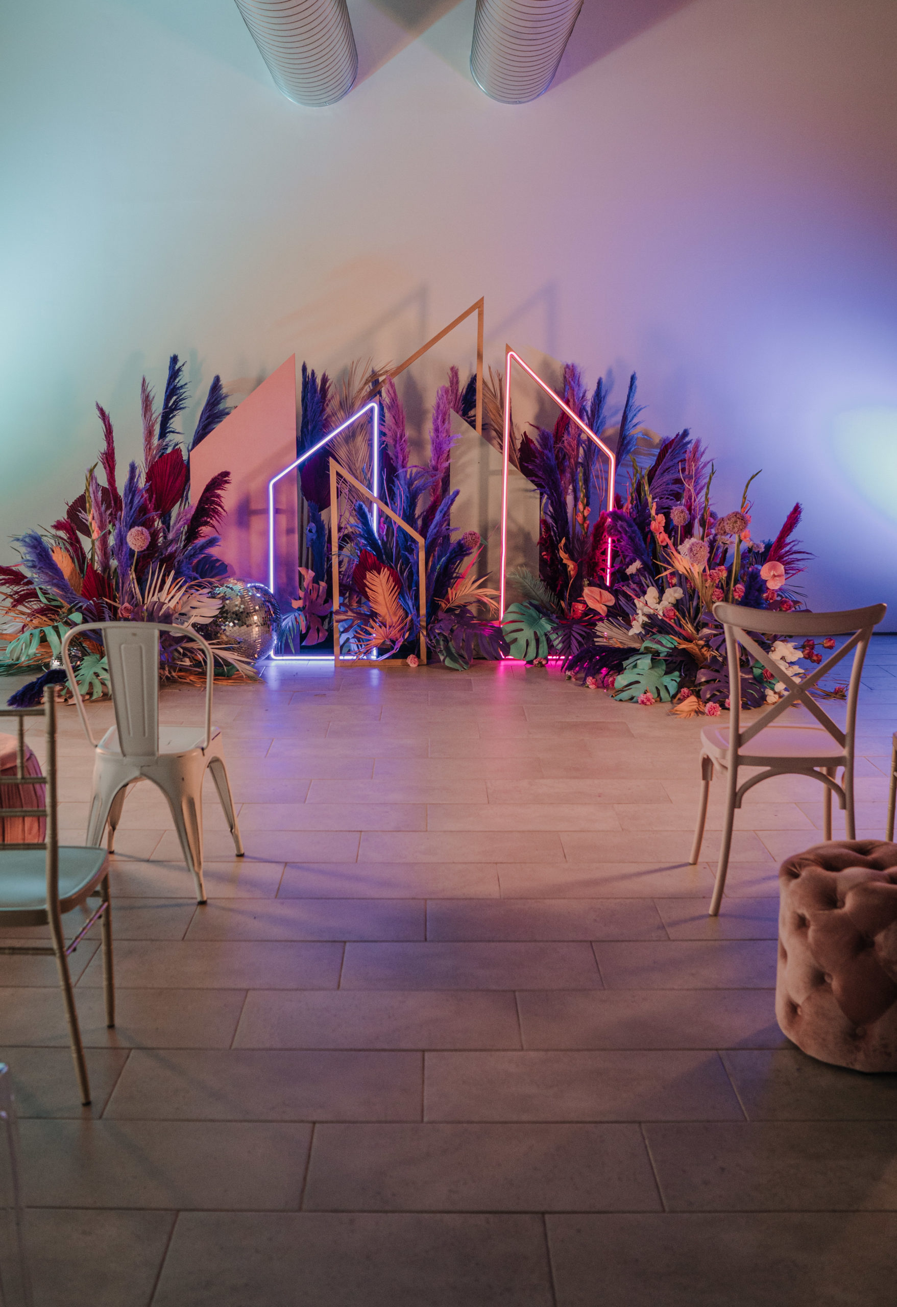 Ceremonia nupcial colorida con flores, sillas, taburetes y neones