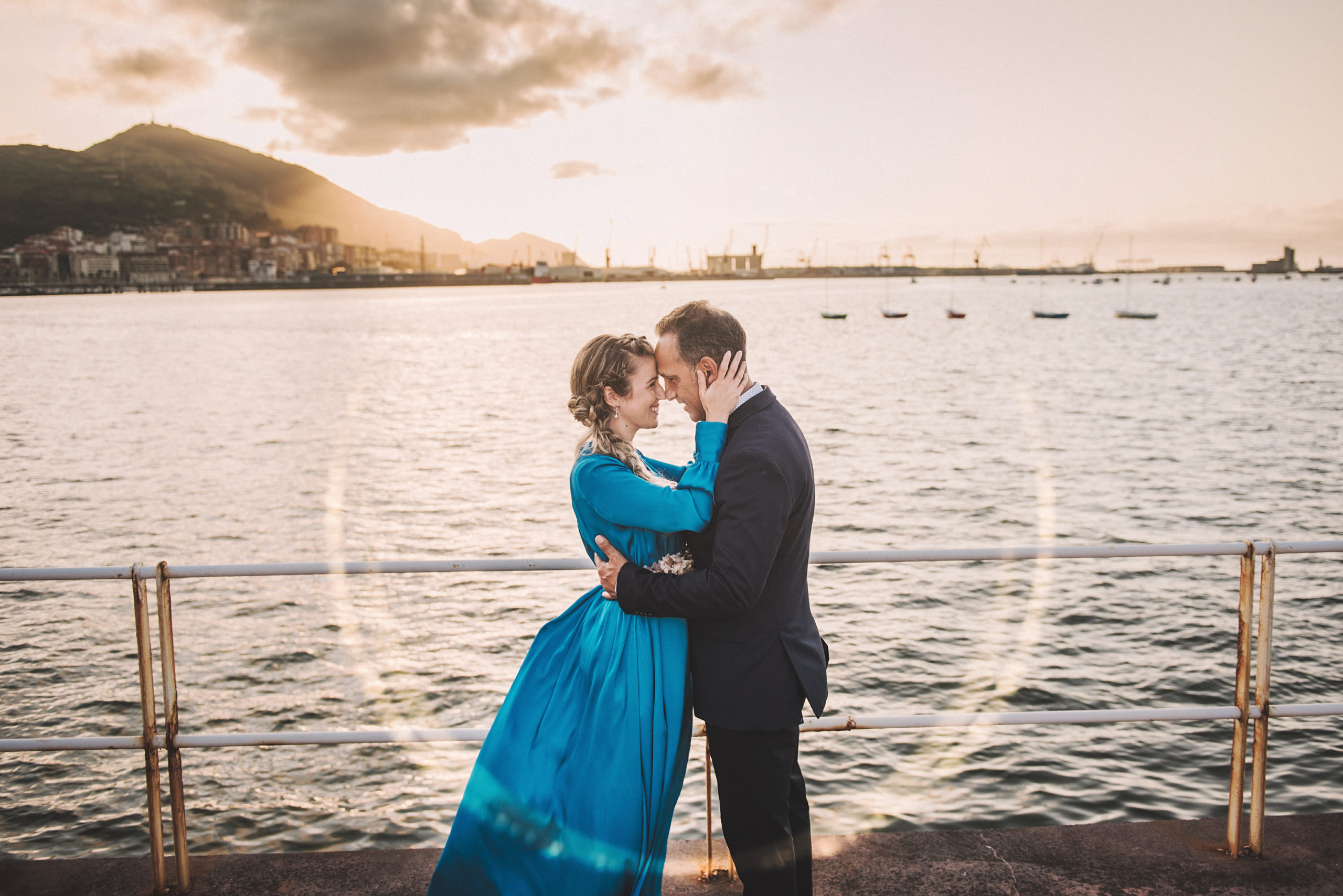 Novios posando en el embarcadero frente al mar al atardecer.