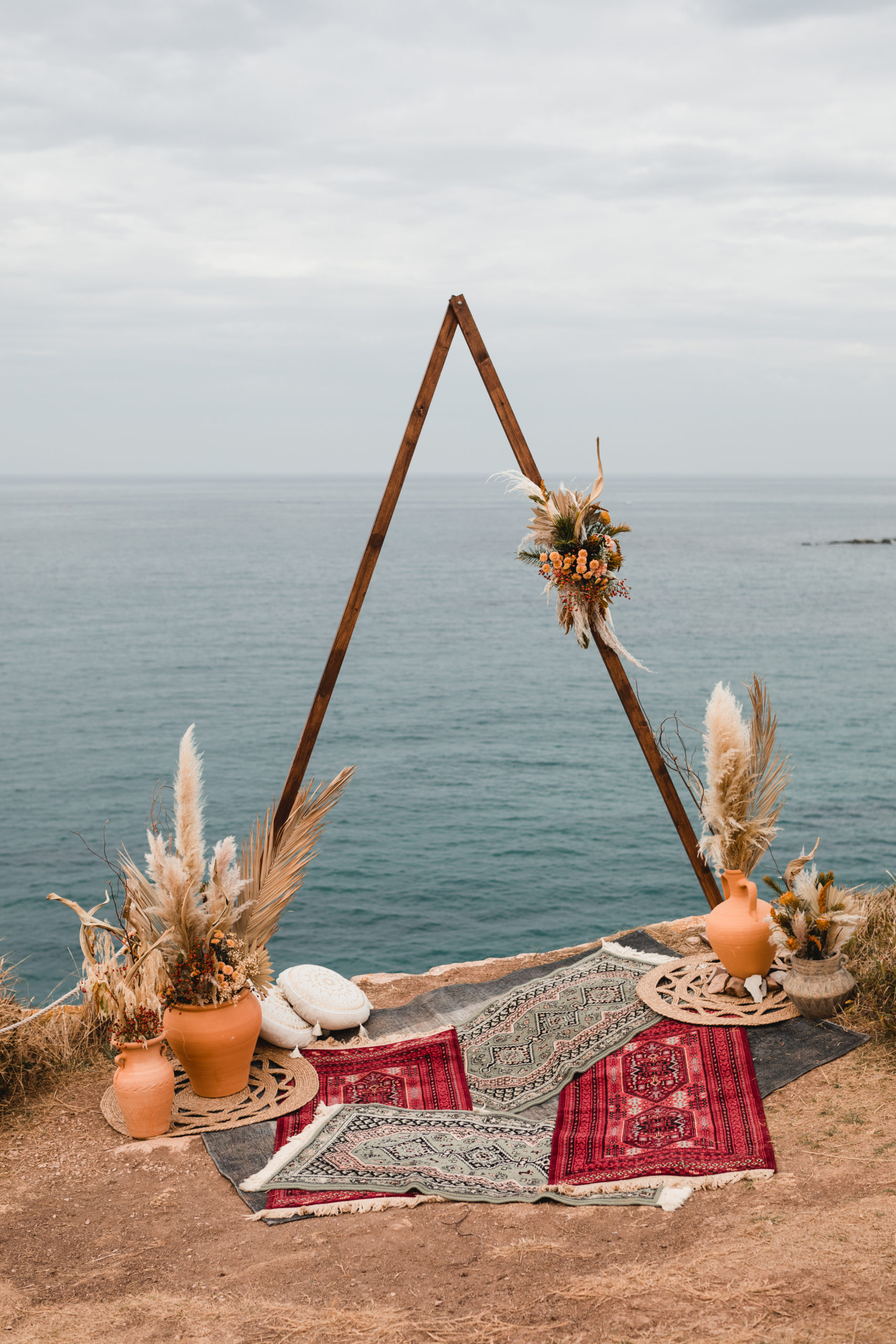 Ceremonia nupcial con arco, alfombras, cojines, jarrones y flores, con el mar de fondo