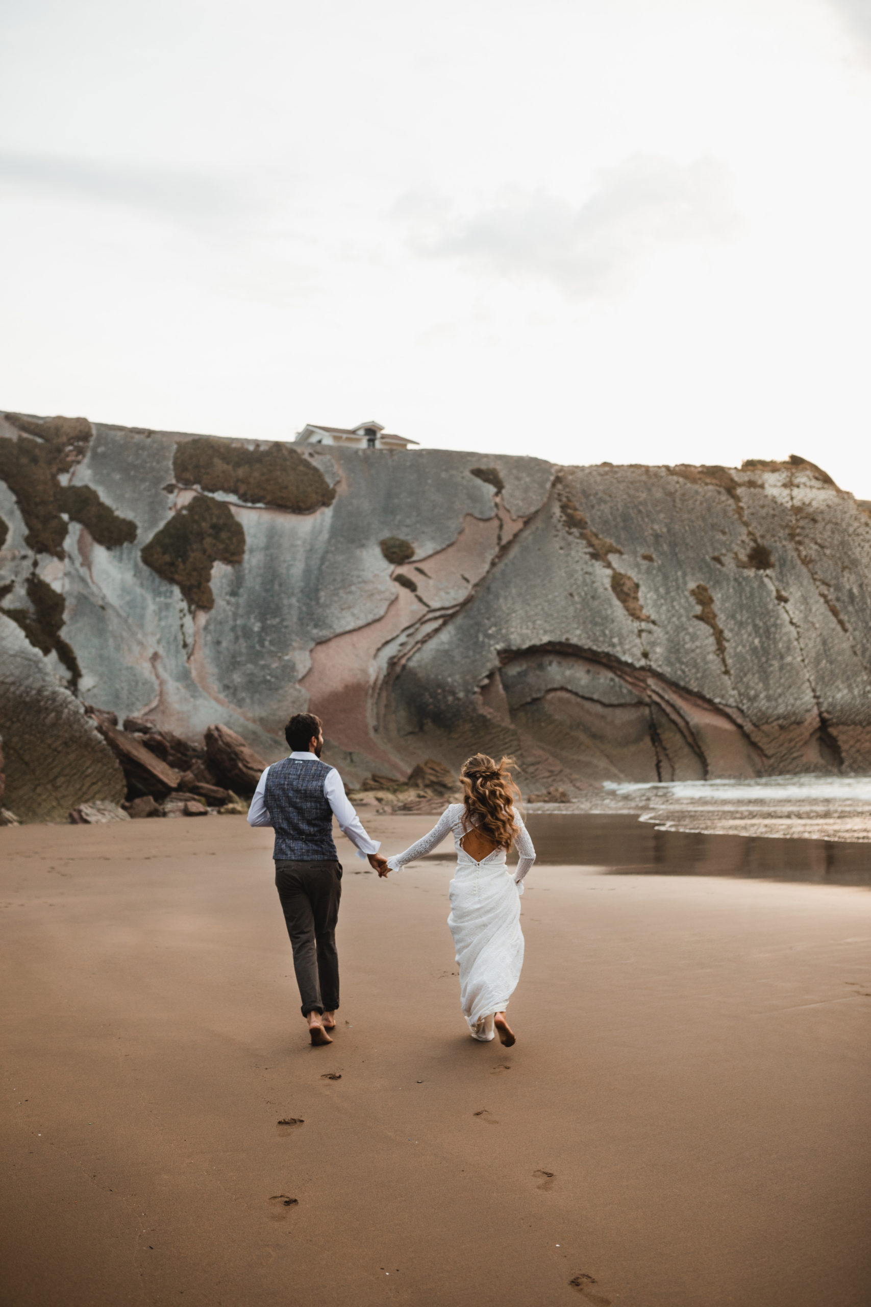 Novio y novia corriendo por la playa de Zumaia el día de su boda