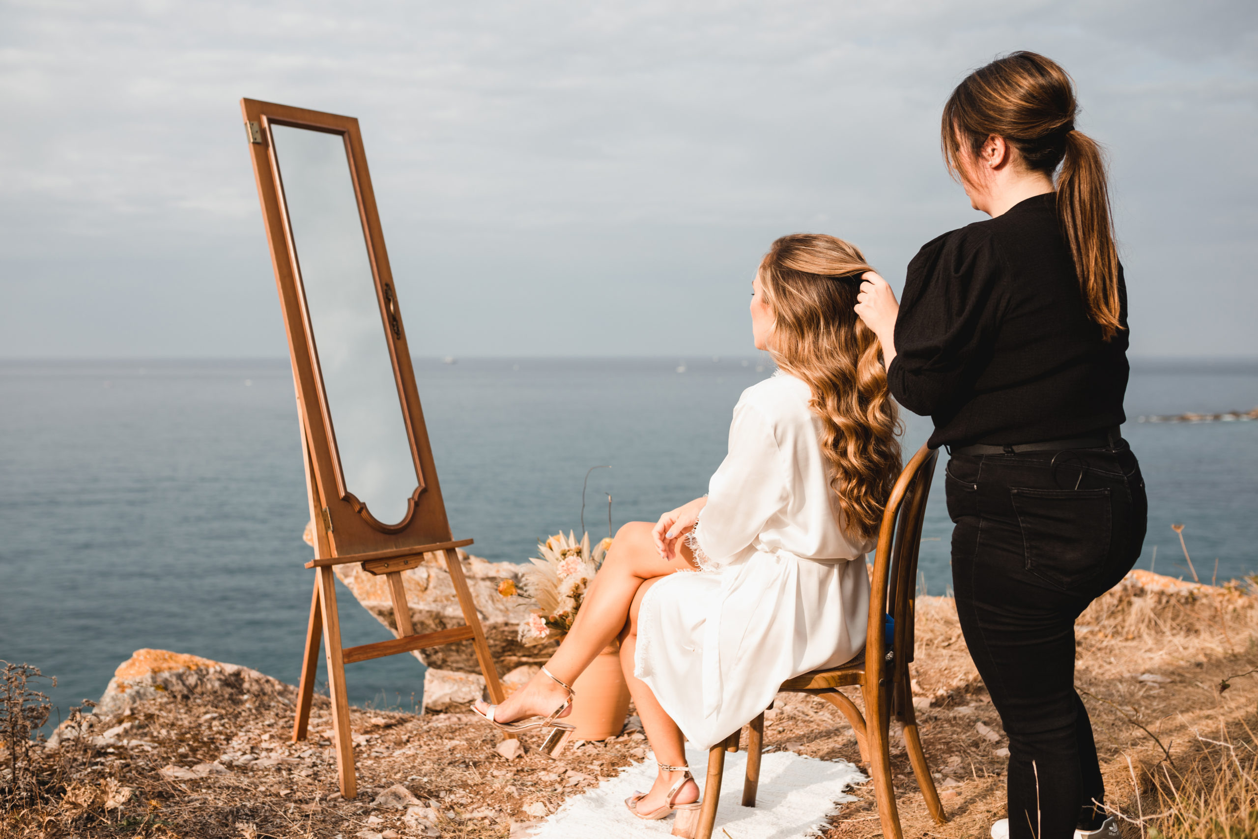 Peluquera peindando a la novia el día de su boda en la montaña con el mar de fondo