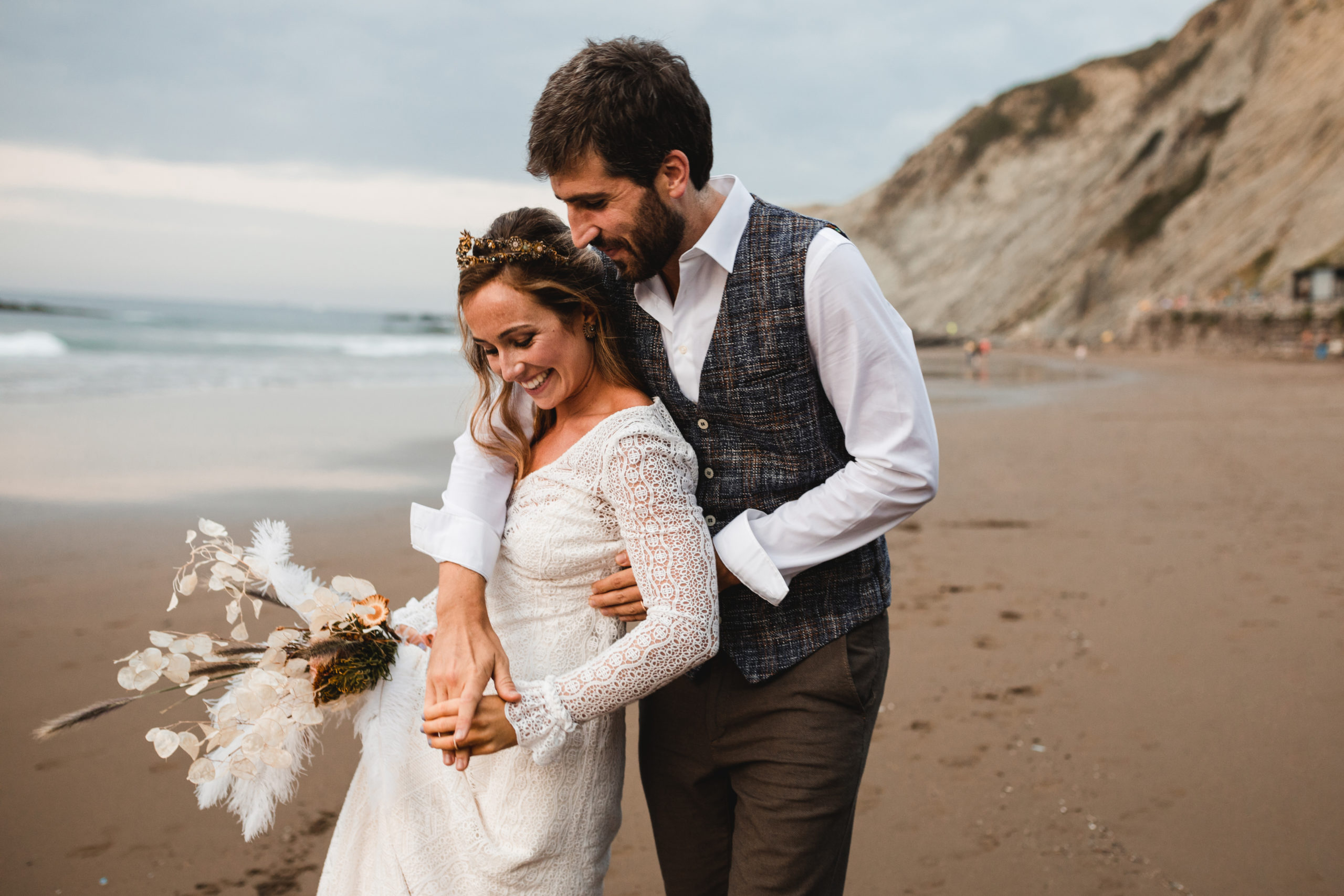 Novio abraza a la novia con sus brazos en la playa de Zumaia