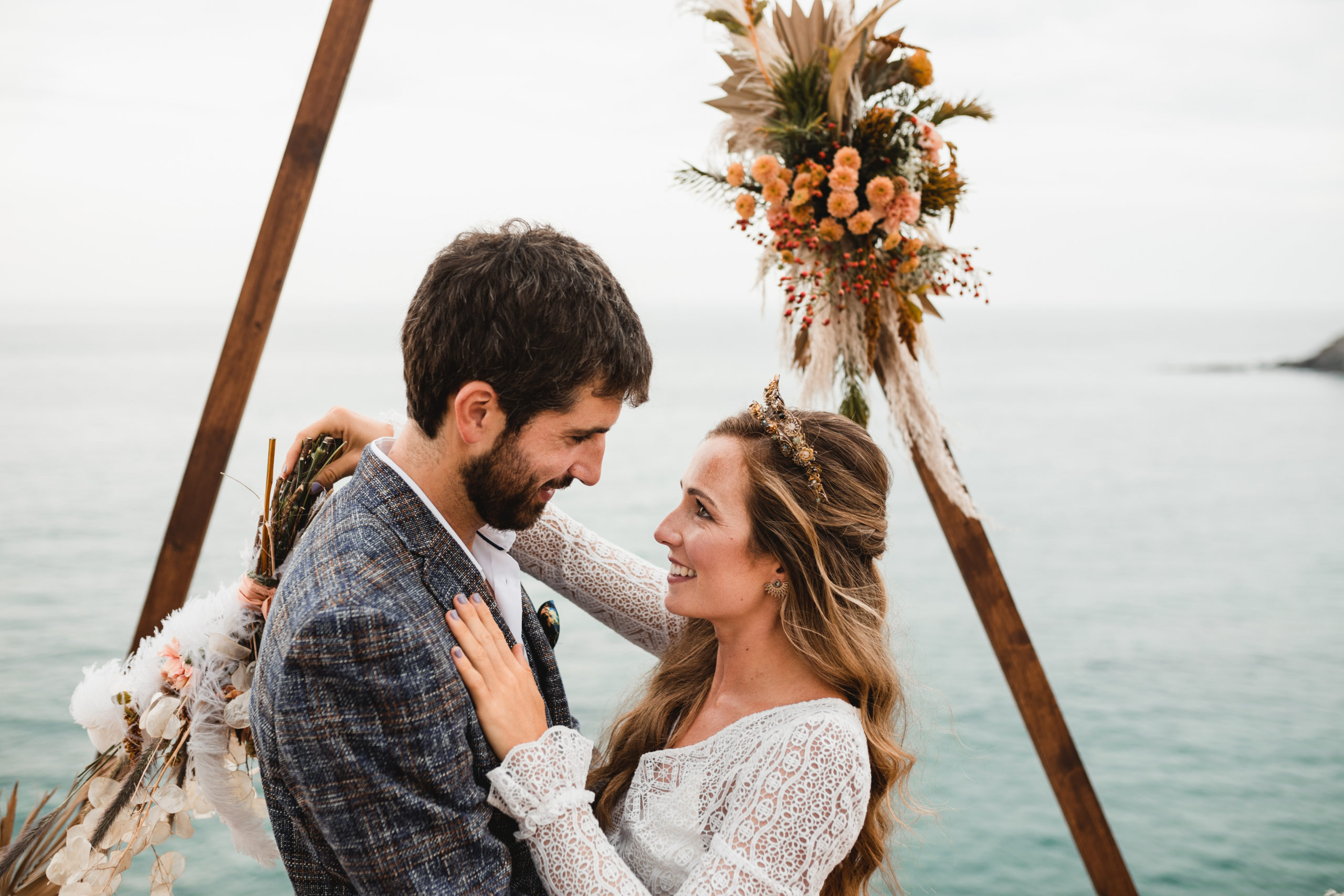Mirada de la novia al novio con el mar y el arco nupcial de fondo