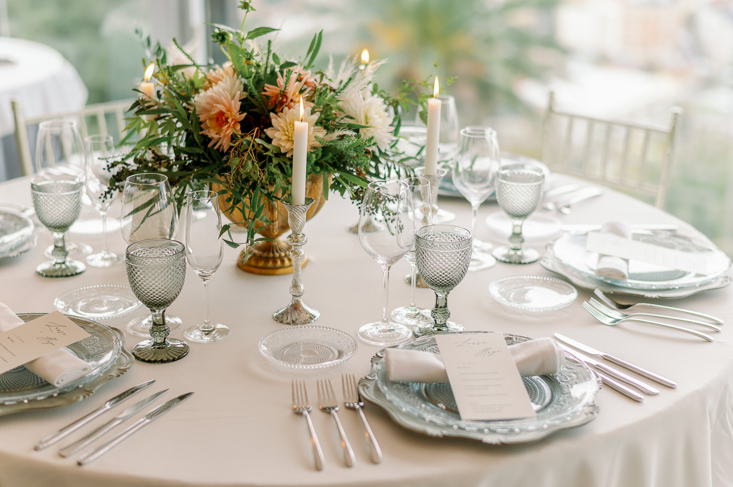 Mesa con bajoplatos, cubertería, copas, candelabros y platos de pan y minutas