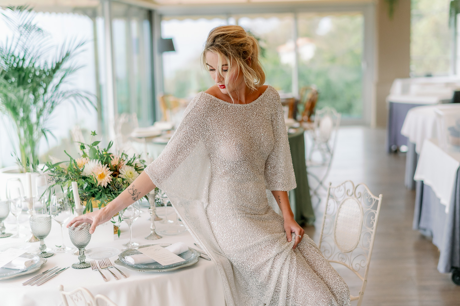 Novia sentada en la mesa con vestido de novia coge una copa gris en el Mirador de ulia