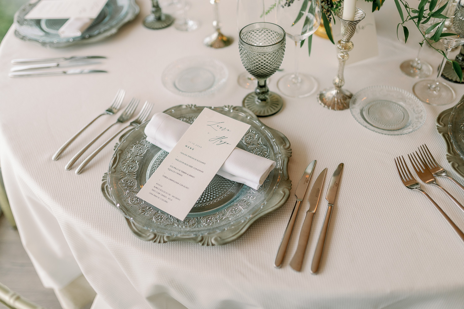 Mesa con bajoplatos, cubertería, copas, candelabros y platos de pan y minutas