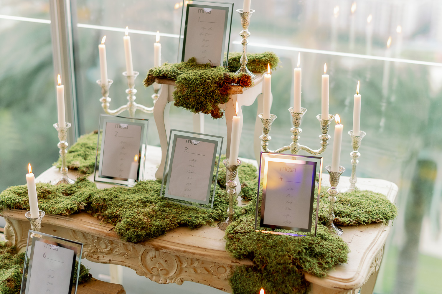 Seating plan con mesas blancas, candelabros, velas y musgo