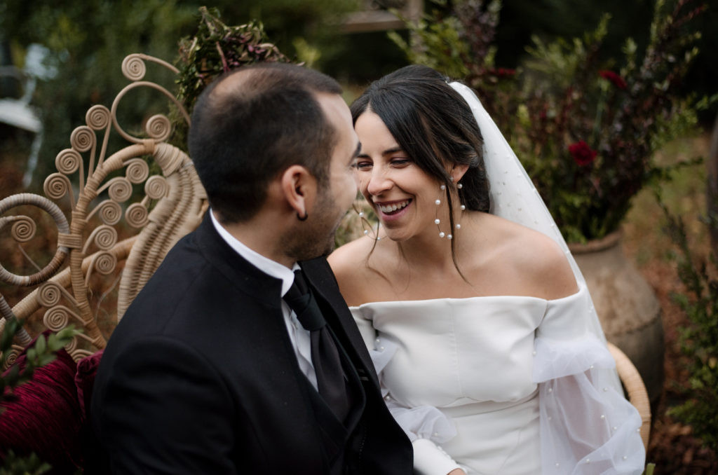 Novia y novio sentados en el sillón ratán pavo real en la ceremonia nupcial