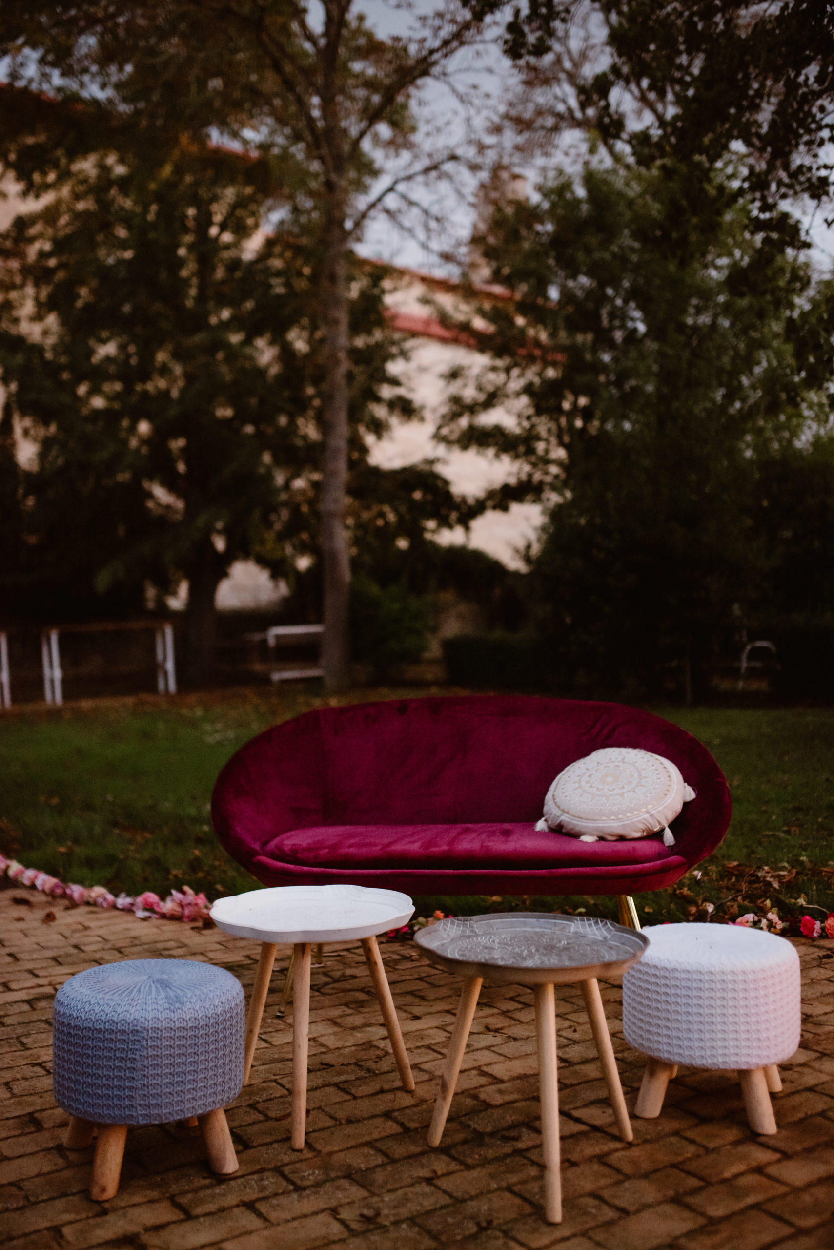 Sillón de terciopelo granate, mesa auxiliar de madera y puff gris y blanco